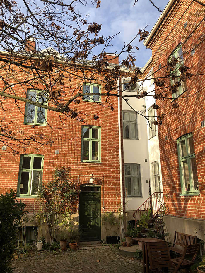 Foto på innergård med hus i rött tegel och vit puts, om hösten.